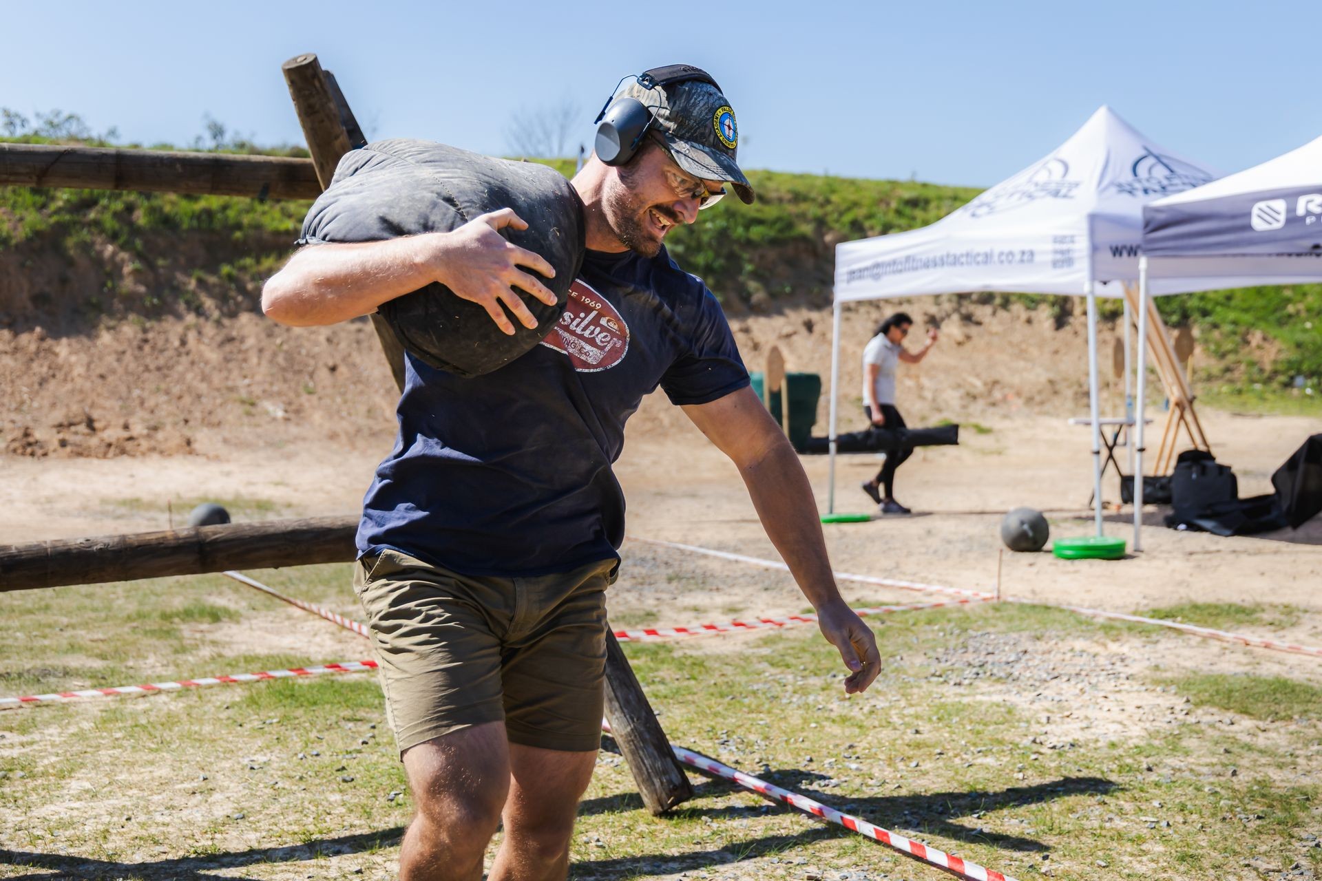 Man carrying a heavy sandbag on his shoulder during an outdoor strength challenge event.