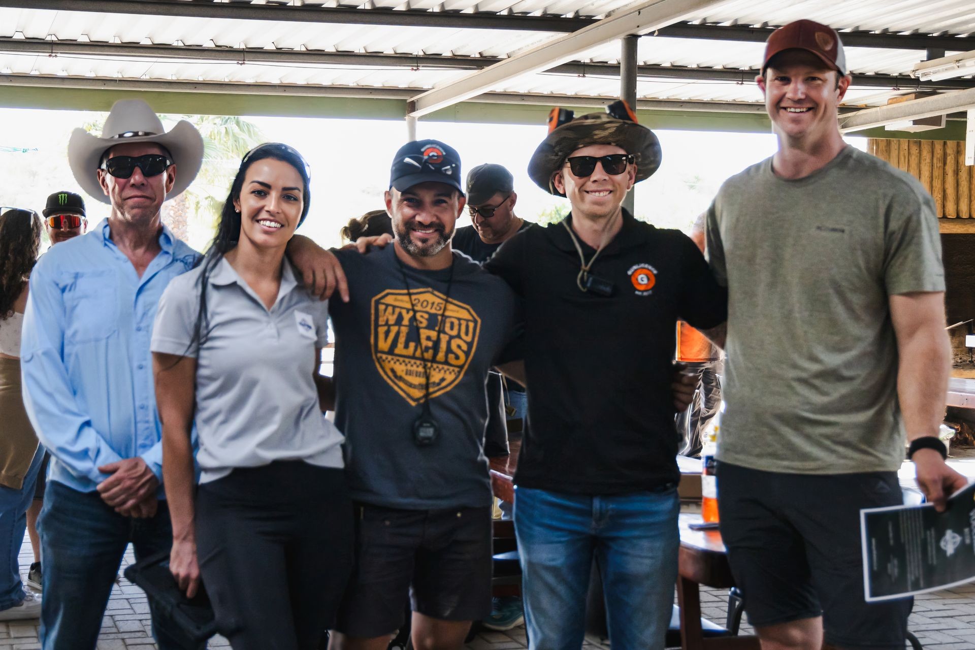 Group of five people wearing casual and outdoor gear posing under a shaded area.
